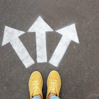 Woman standing near arrows on asphalt, top view. Choice concept